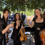 Professional string trio performing live at an outdoor garden wedding in Sydney. Three female musicians playing violin, viola, and cello during a wedding ceremony.