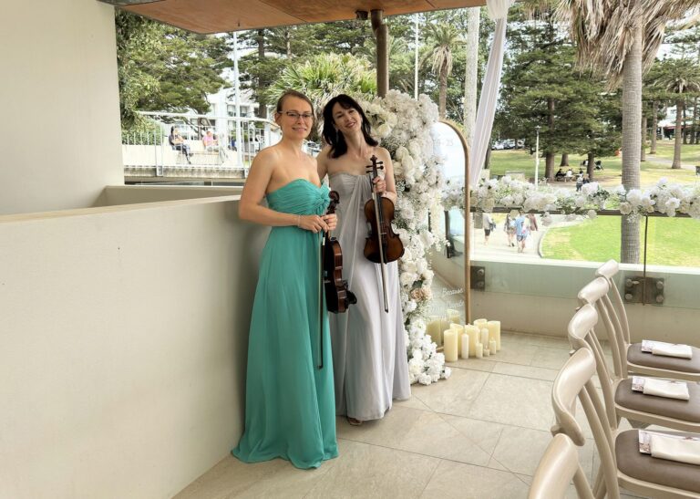 Professional female violin duo in elegant gowns performing live music for an outdoor event in Sydney.