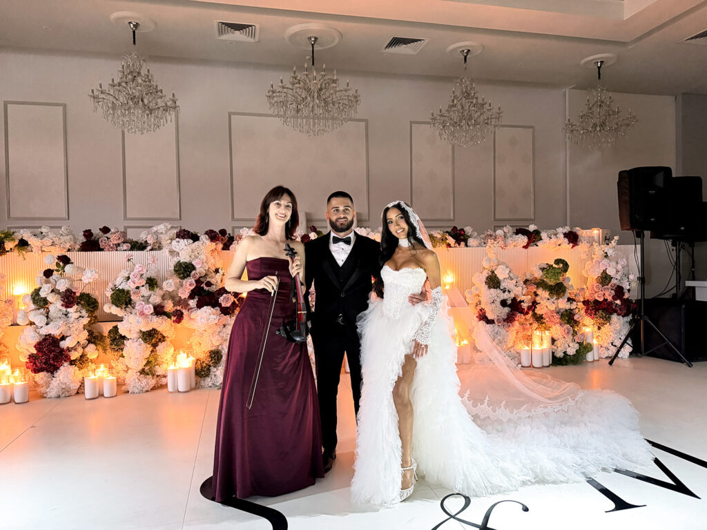Professional electric violinist in a burgundy dress performing at a luxury wedding reception in Sydney next to a bride and groom.