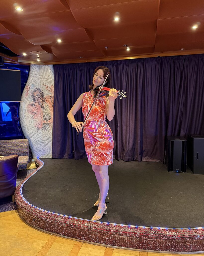 Professional female violinist in a white dress performing at an indoor event venue with warm ambient lighting.