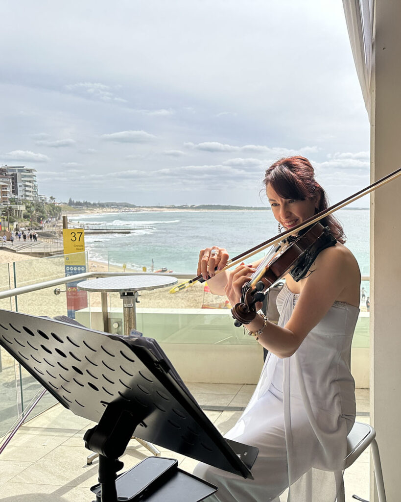 A professional female violinist in a white dress performing a solo classical piece during an event.
