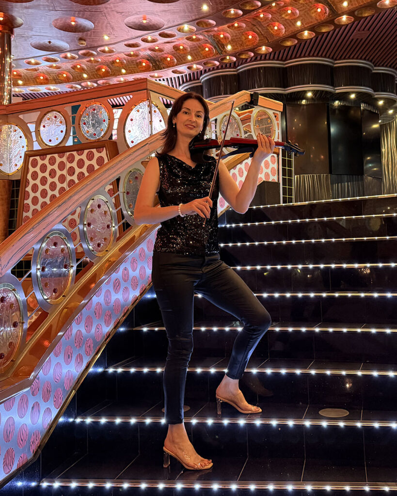 Professional female electric violinist performing solo on an illuminated grand staircase for a corporate event.