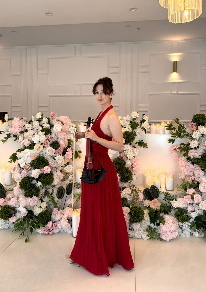 Professional female wedding and event violinist in a red dress playing live music at a beautifully decorated Sydney venue.