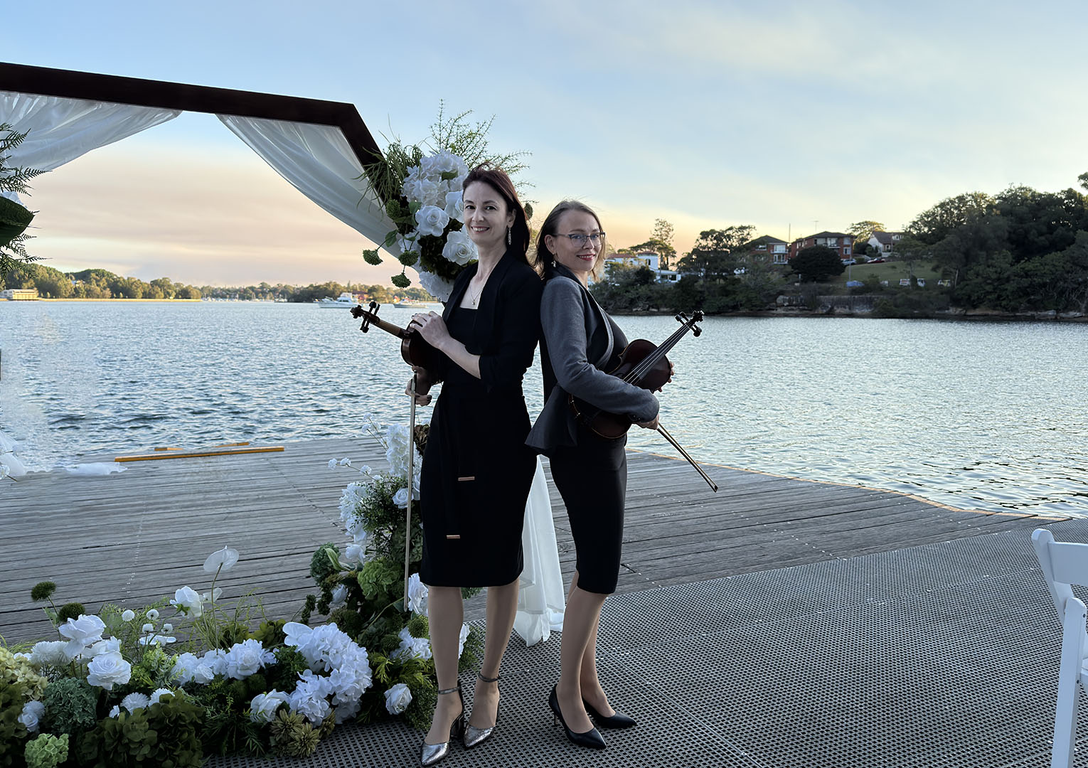 Professional female violin duo performing live at a waterfront outdoor event in Sydney.