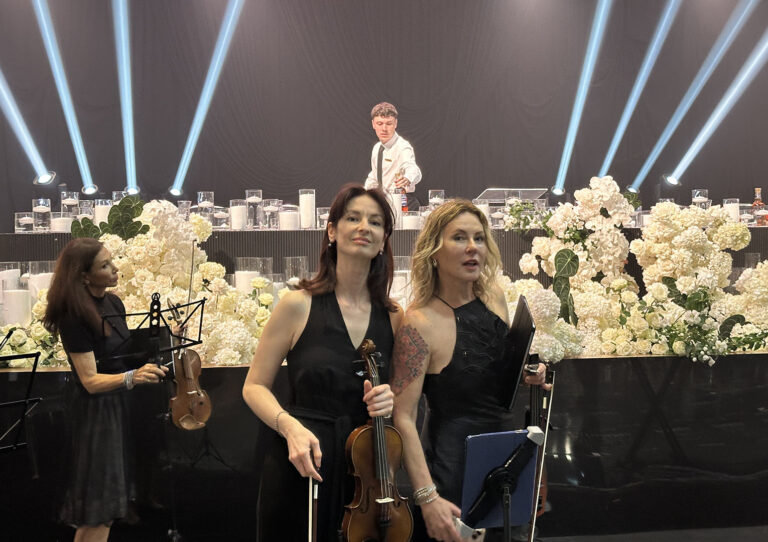 Live wedding music performance featuring a professional string duo with two female violinists playing at a beautifully decorated reception venue.