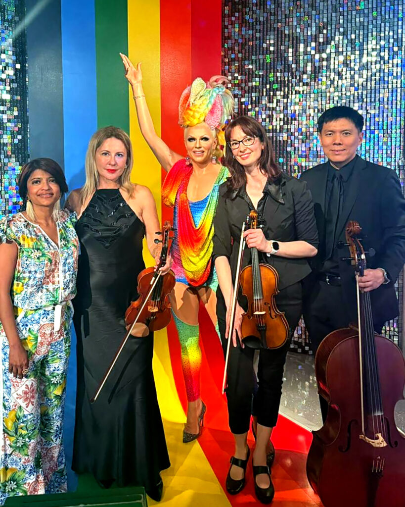 Live corporate event string ensemble posing with a colourful performer at a Madame Tussauds Sydney business event.