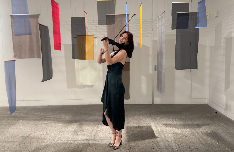Solo female violinist in a black dress playing at a corporate event in a modern art gallery.