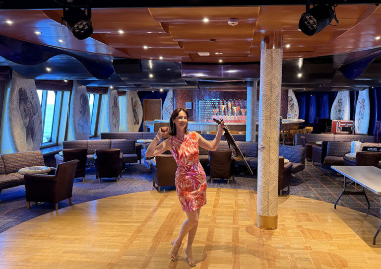 A female solo violinist in a pink dress performing live with an electric violin on an indoor stage at a birthday party event.