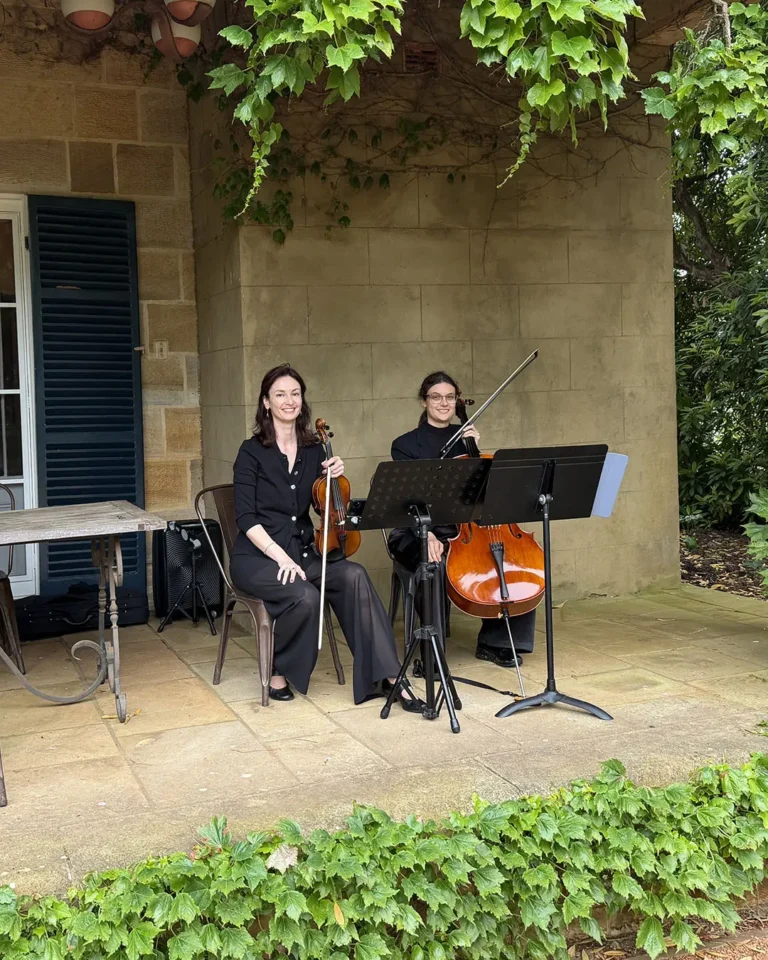 Professional violin and cello duo performing live classical music for an outdoor garden wedding ceremony.