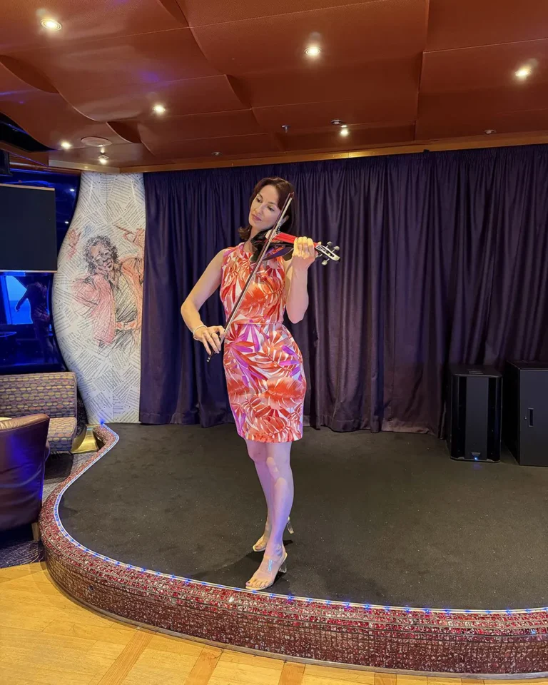 Professional female violinist in a white dress performing at an indoor event venue with warm ambient lighting.