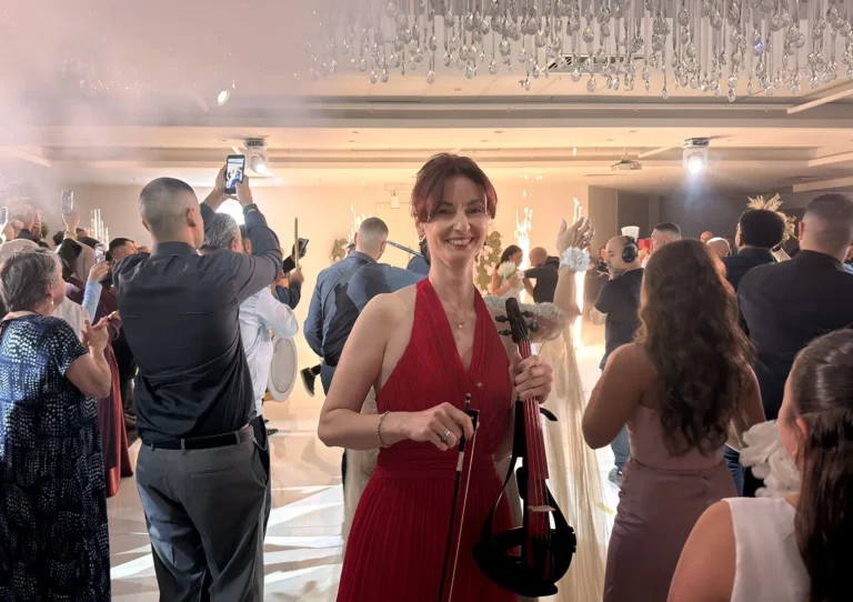 Guests celebrating at a luxury wedding reception, featuring a smiling woman in a red gown holding an electric violin.