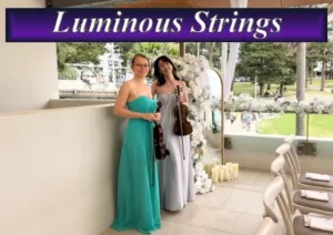 Two female musicians from Luminous Strings performing with a violin and cello at a bright outdoor event venue.