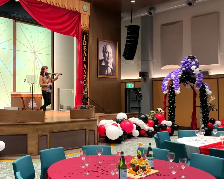 Solo female violinist performing on stage with professional sound equipment at a decorated event hall venue.