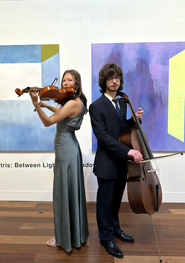 Classical string duo with female violinist and male cellist posing in front of modern artwork for a PlanEvent ensemble guide.